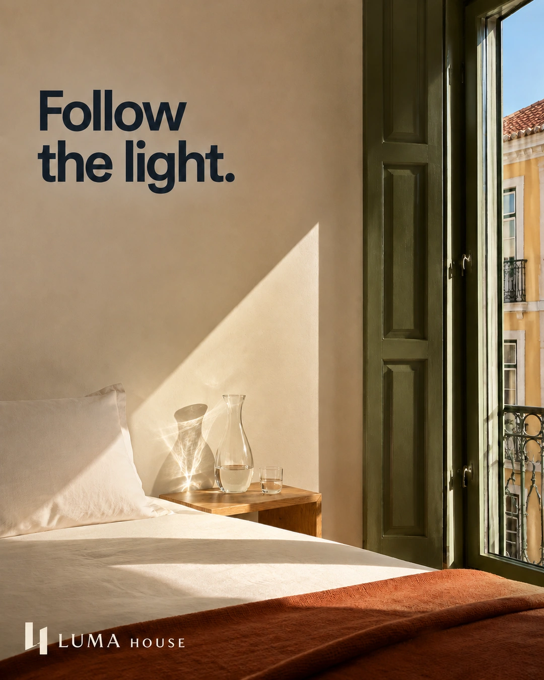 A diagonal beam of sunlight and glass-carafe caustics fall across hotel linen and a pale wall.